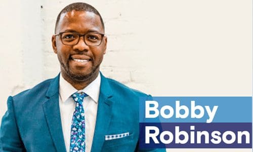 bobby robinson is smiling in front of a blue wall