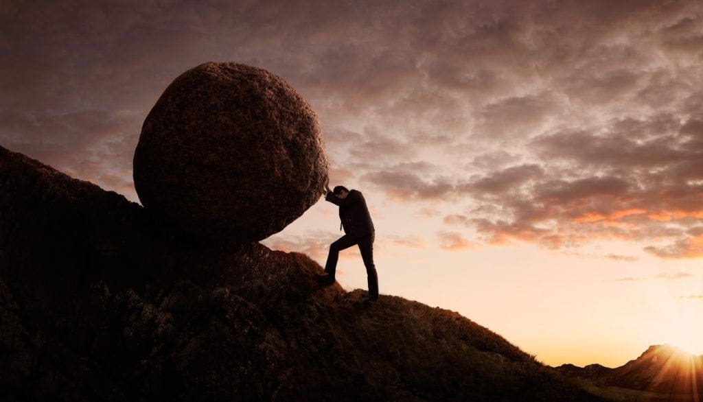 A man pushing a round rock on a hill