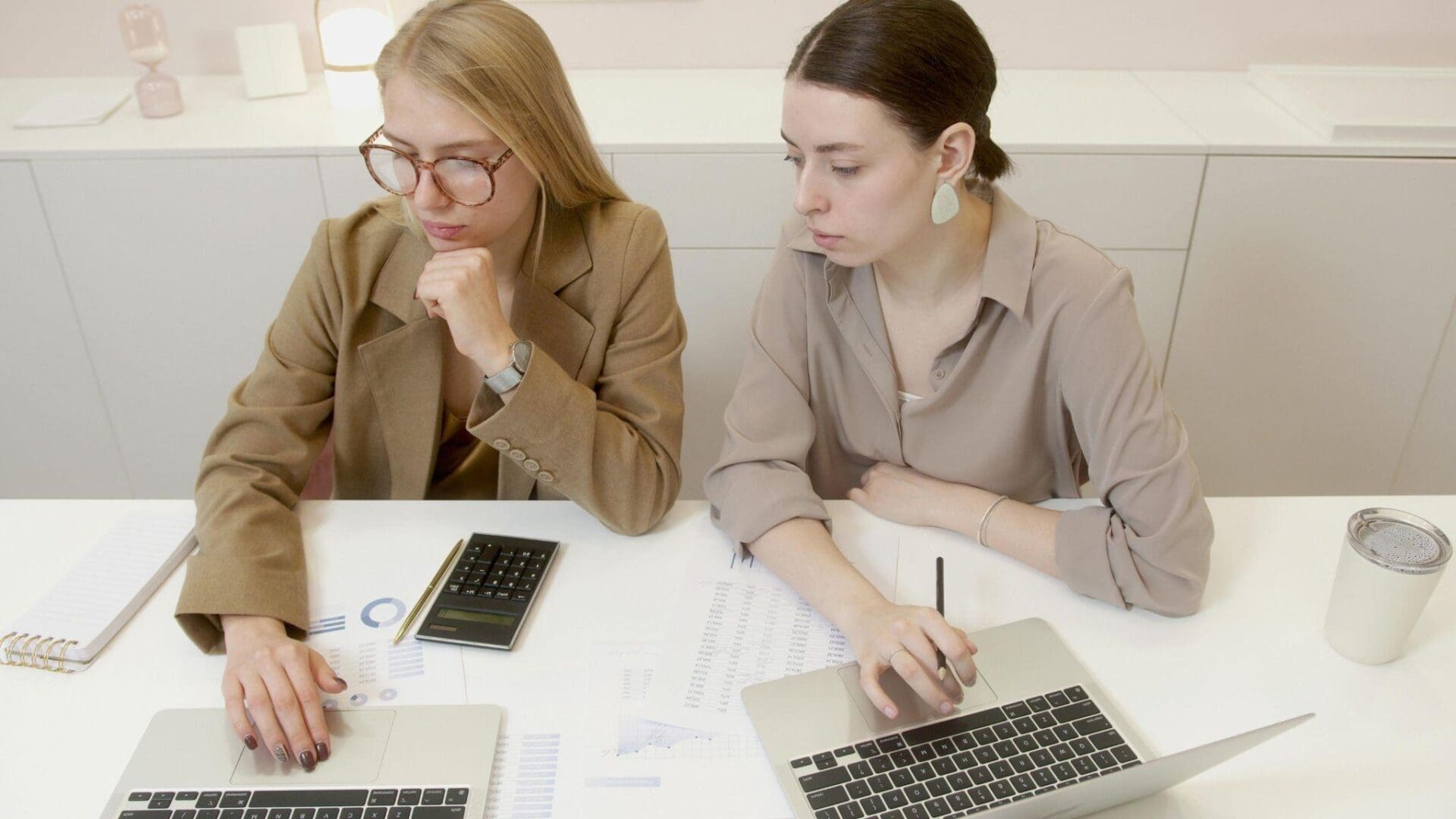 Two professionals in suits review a laptop during a meeting.
